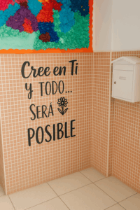 Buzón blanco con mural y mensaje motivador “Cree en ti y todo será posible” en el pasillo del colegio.